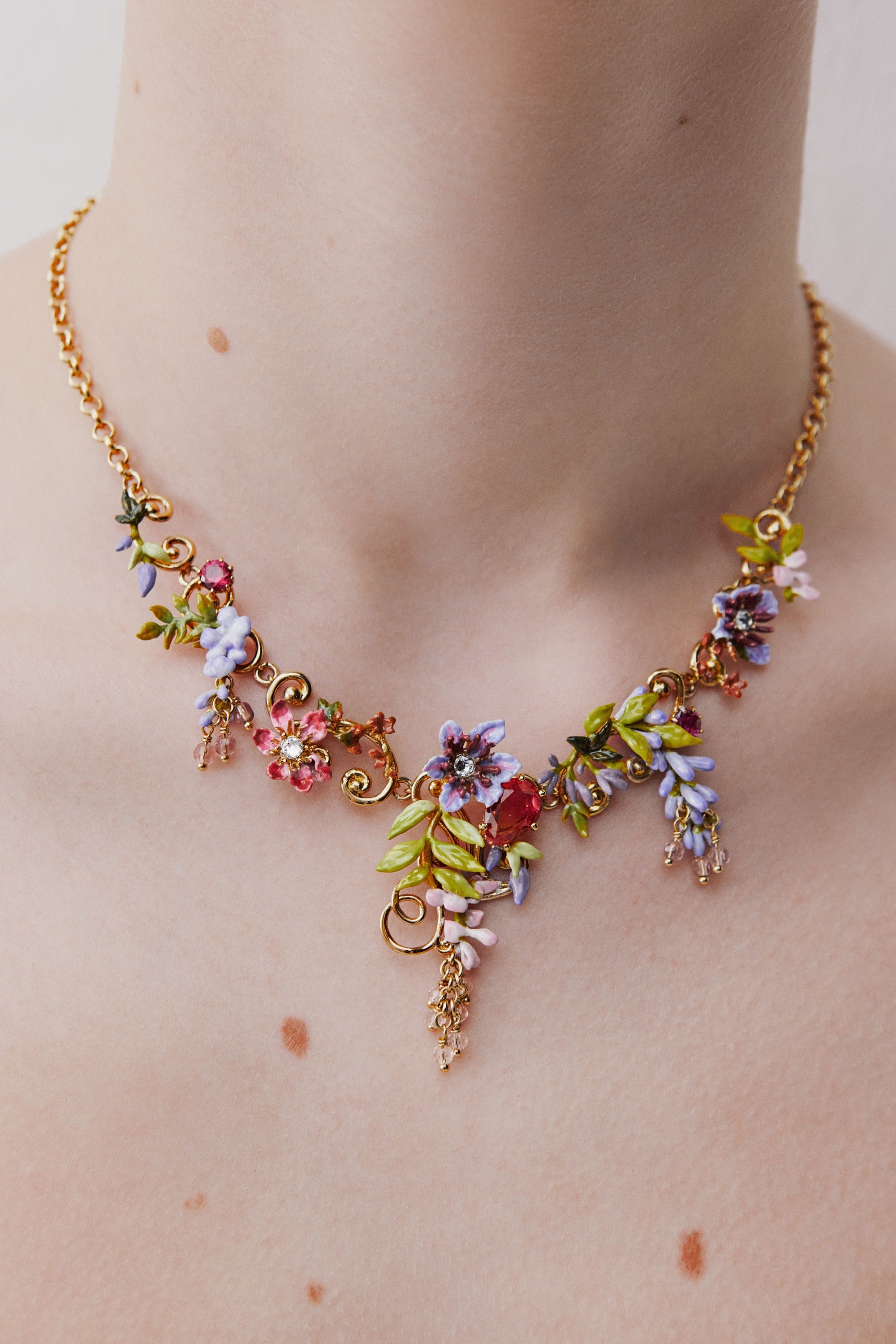 Statement necklace with pink and purple wisteria on a golden arabesque, adorned with ivy and dangling faceted pink crystal beads